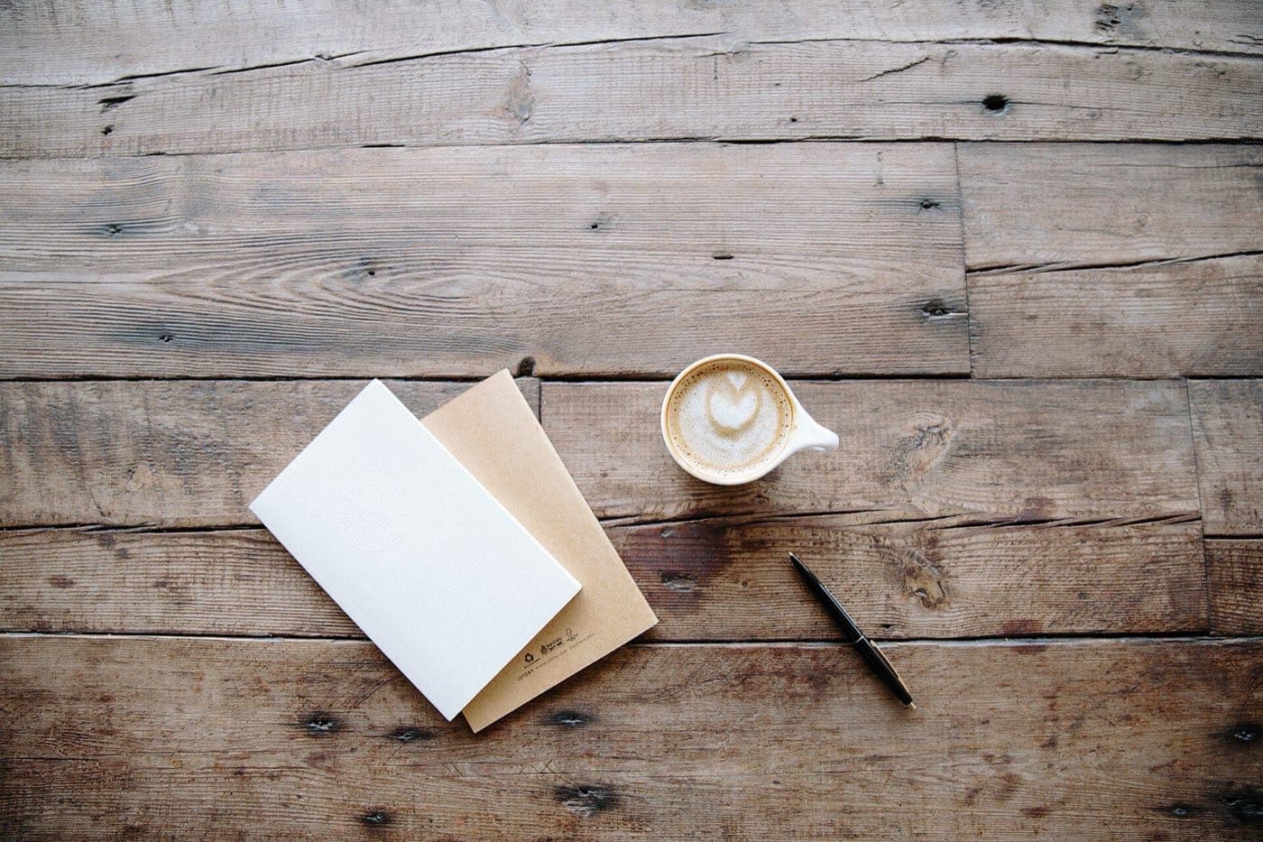 Two notebooks, a pen, and a cup of coffee on a rustic wooden table