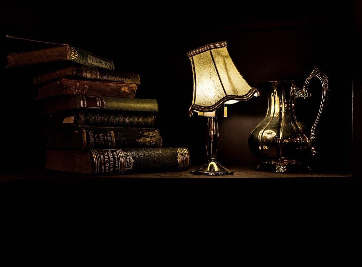 A stack of old books beside a lit desk lamp