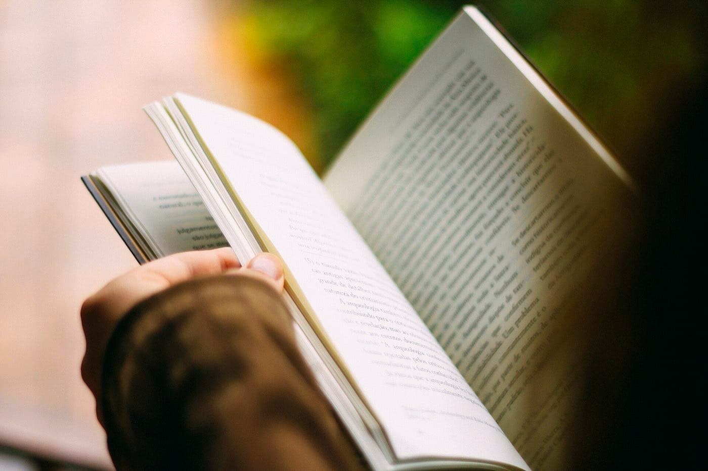 A hand leafing through the pages of a paperback book