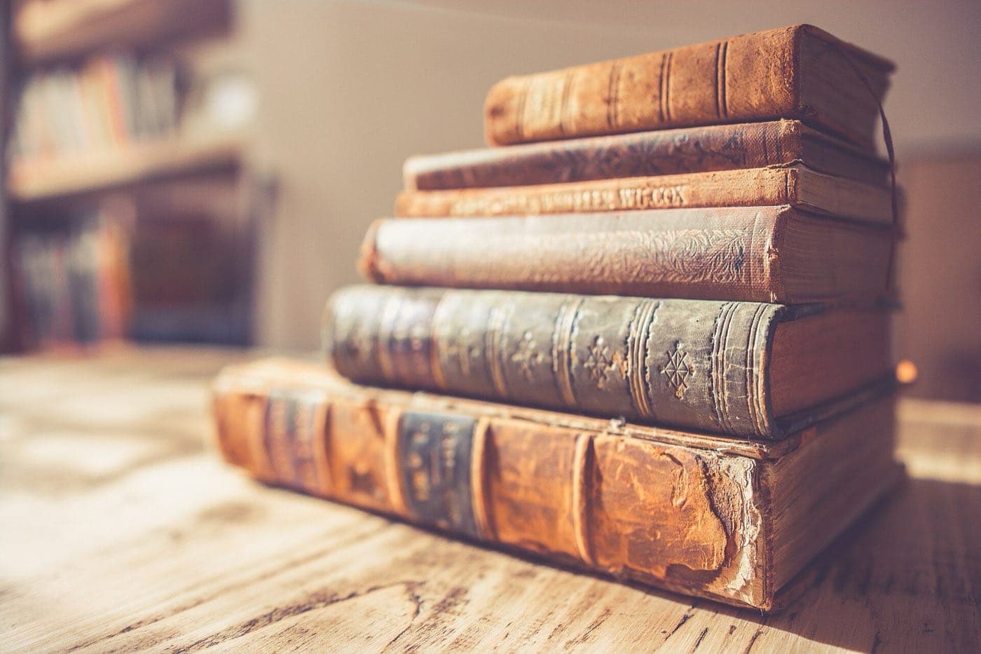 A stack of worn leather-bound books on a wooden table in a library