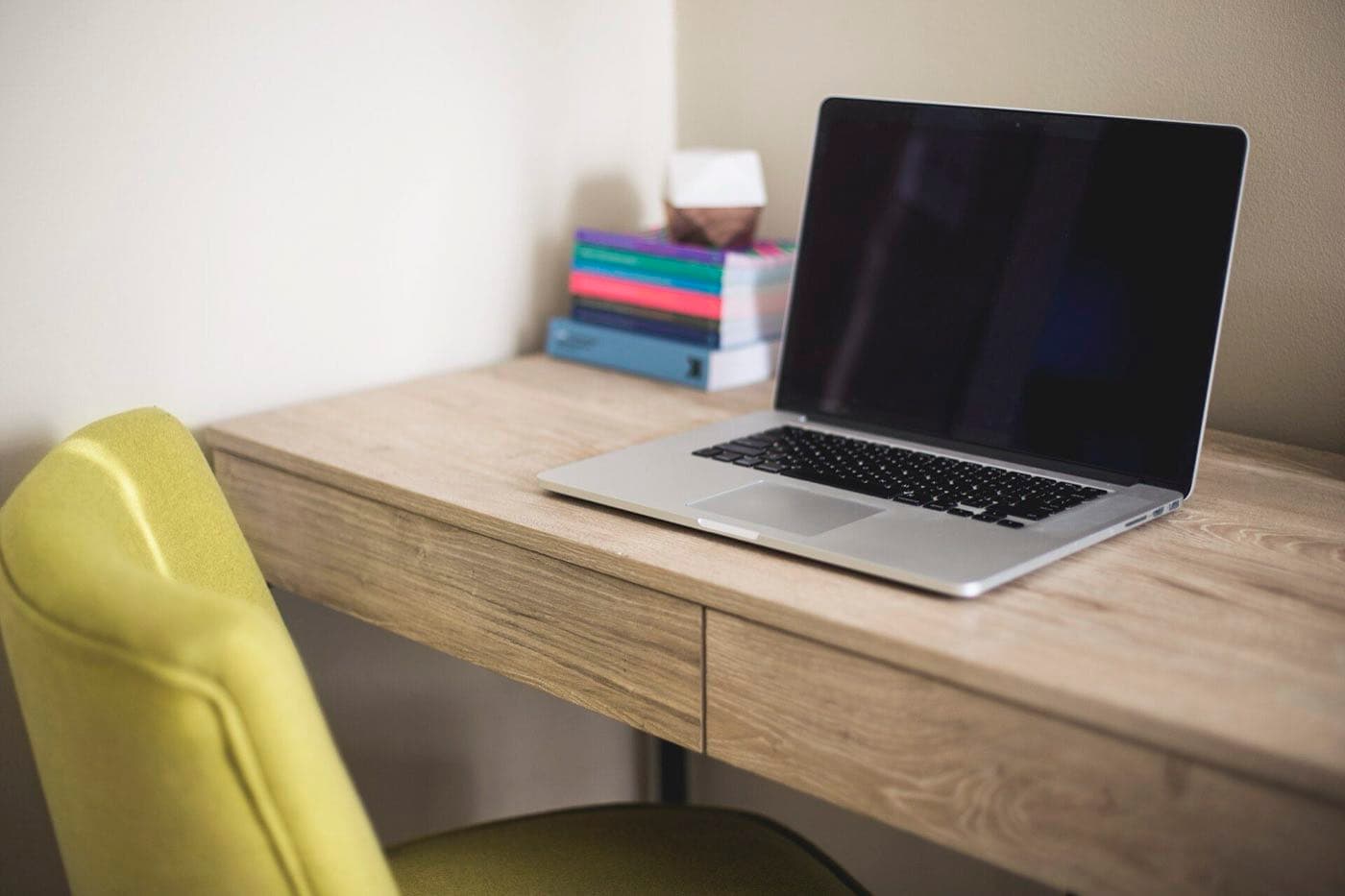An open laptop on a wooden desk beside a stack of books