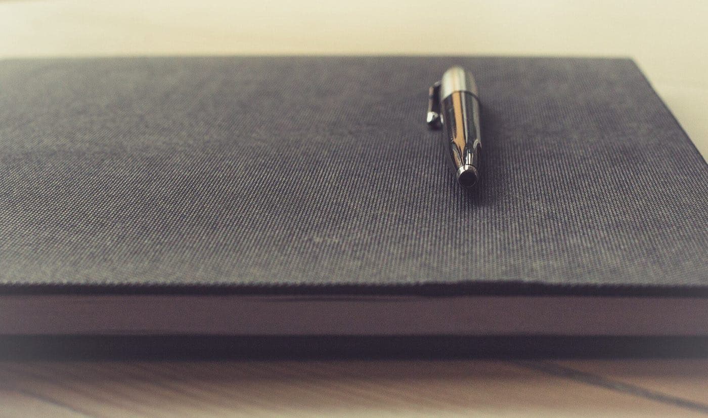 A pen resting on a closed hardcover notebook